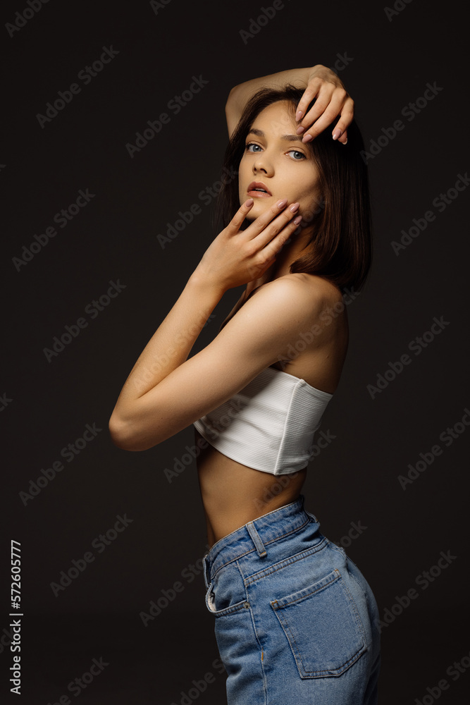 young woman in a white tank top and denim shorts on a dark background young woman in a white tank top and denim shorts on a dark background