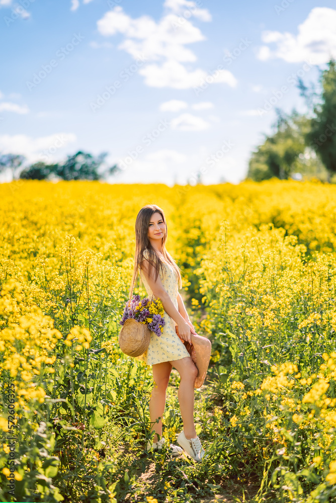 girl is standing in a yellow field of rapeseed. A woman with a bouquet of flowers in a bag and a hat