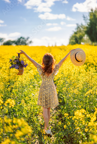 girl with flowers and a hat in a field of rapeseed. Yellow flower field. View from the back