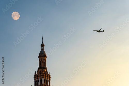 Airplane flying over Seville at sunset with a full moon. Holidays concept