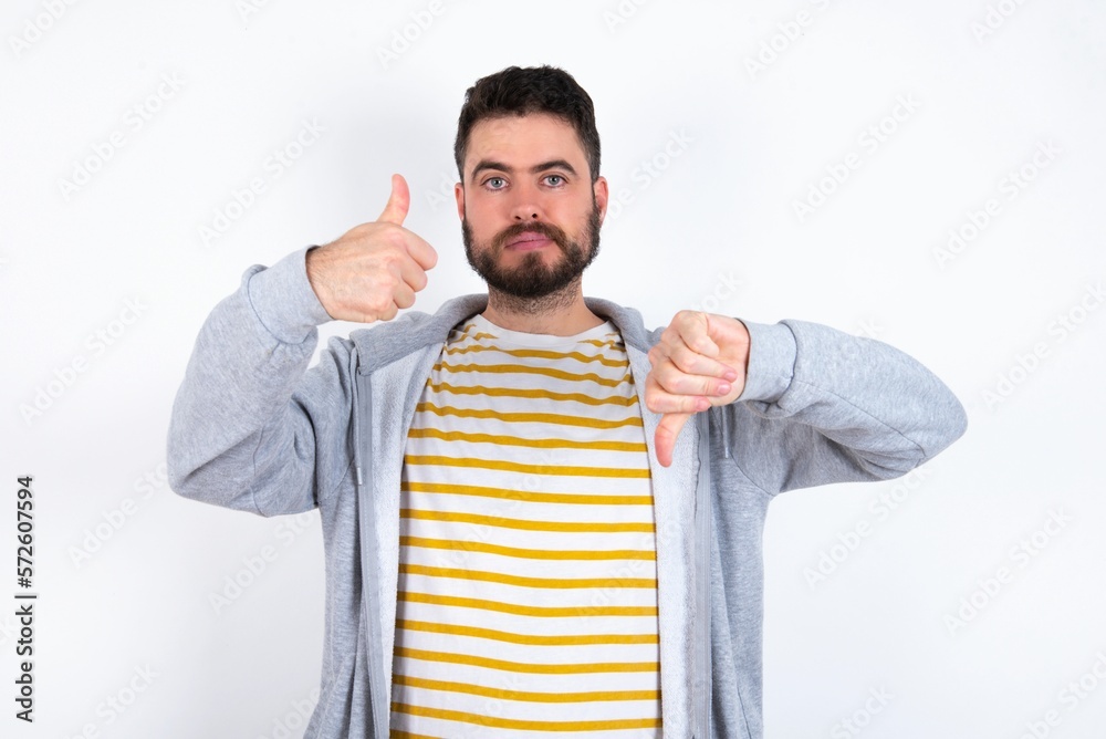 caucasian man wearing casual sportswear over white wall showing thumbs up and thumbs down, difficult choose concept caucasian man wearing casual sportswear over white wall showing thumbs up and thumbs down, difficult choose concept