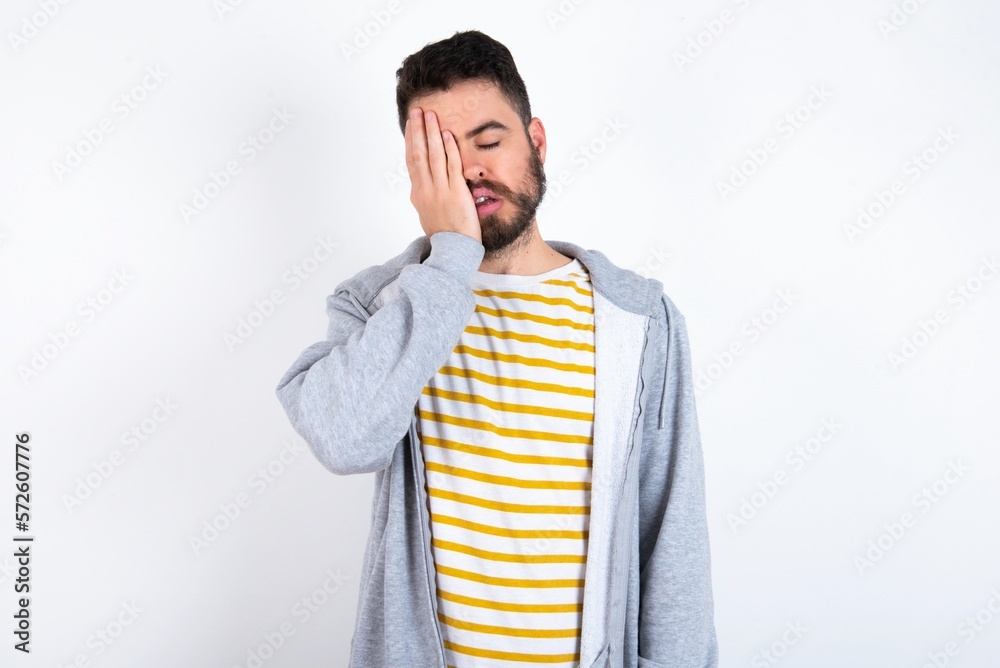 Tired overworked caucasian man wearing casual sportswear over white wall has sleepy expression, gloomy look, covers face with hand, has eyes shut, gasps from tiredness, fatigue after party Tired overworked caucasian man wearing casual sportswear over white wall has sleepy expression, gloomy look, covers face with hand, has eyes shut, gasps from tiredness, fatigue after party