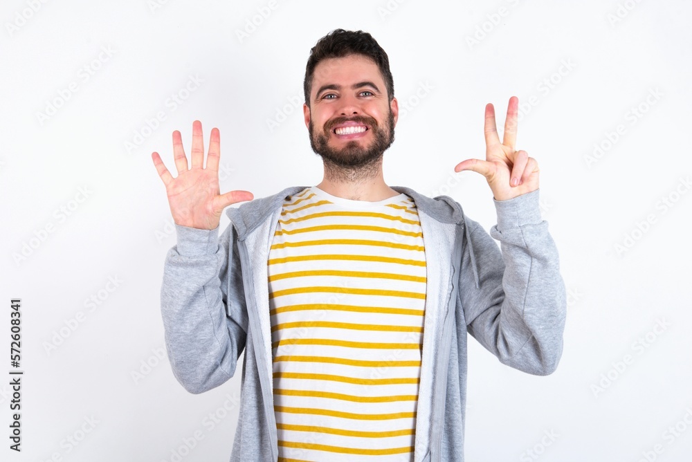 caucasian man wearing casual sportswear over white wall showing and pointing up with fingers number eight while smiling confident and happy. caucasian man wearing casual sportswear over white wall showing and pointing up with fingers number eight while smiling confident and happy.