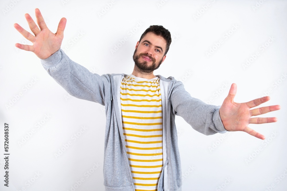 Naklejka premium caucasian man wearing casual sportswear over white wall looking at the camera smiling with open arms for hug. Cheerful expression embracing happiness.