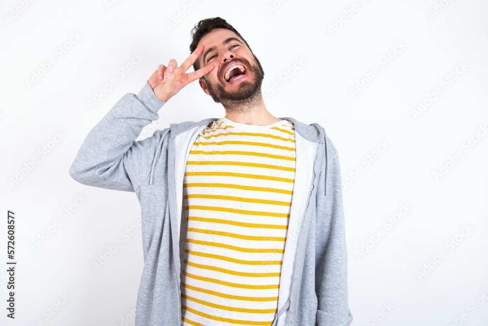 caucasian man wearing casual sportswear over white wall Doing peace symbol with fingers over face, smiling cheerful showing victory caucasian man wearing casual sportswear over white wall Doing peace symbol with fingers over face, smiling cheerful showing victory