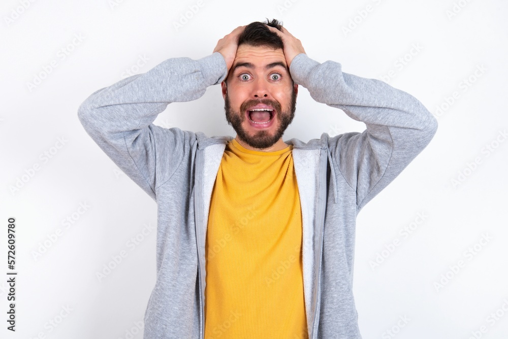 Cheerful overjoyed caucasian man wearing casual sportswear over white wall reacts rising hands over head after receiving great news. Cheerful overjoyed caucasian man wearing casual sportswear over white wall reacts rising hands over head after receiving great news.