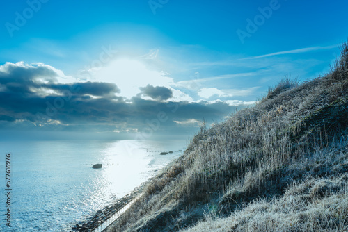 Cold, early morning view of a sloping cliff covered with frost. A distant snow storm is seen on the horizon, out to sea.