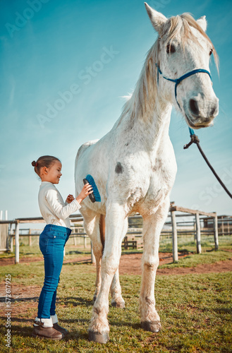 .Girl child, brush horse and outdoor with care, love and holiday at farm, countryside or zoo in summer. Young kid, pet and animal with kindness, friendly and freedom for grooming in morning sunshine.