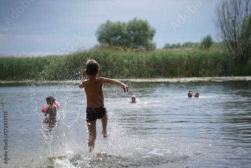 Happy boy run from the shore into the water. Summer childrens vacation on shore of lake or river. kid jump into water, swim and splash around at sunset. Active holidays. Dynamic image. Selective focus