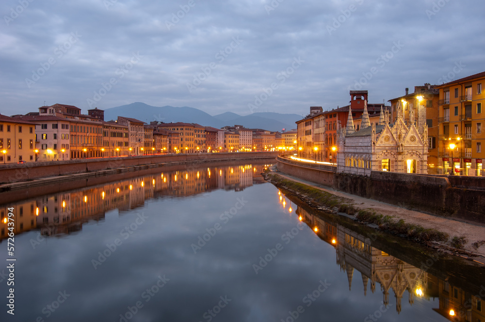 The nightscape of the river Arno and Santa Maria della Spina in Pisa, Italy. Cloud reflection in the river, night lights and mountains in the background