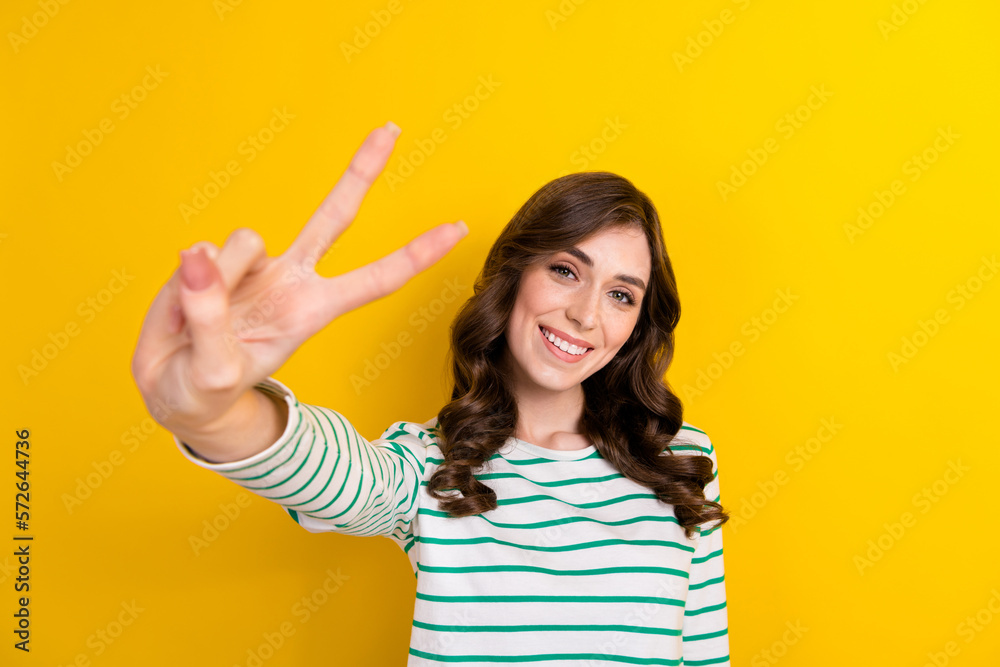 Photo of lovely cheerful girl toothy smile hand fingers demonstrate v-sign isolated on yellow color background Photo of lovely cheerful girl toothy smile hand fingers demonstrate v-sign isolated on yellow color background