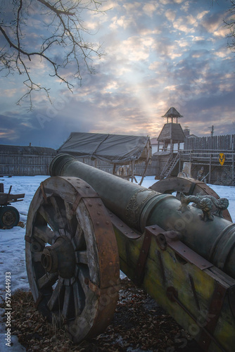 Wooden fortress wall against the sky. Medieval fortress with high walls. Wooden installation in the style of an ancient city. Stockade fence made of logs. Medieval Cannon