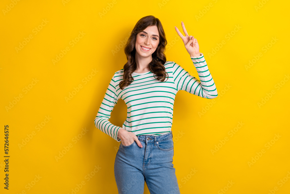 Photo of optimistic cheerful good mood smile youngster woman show v-sign put hand denim jeans friendly person isolated on yellow color background Photo of optimistic cheerful good mood smile youngster woman show v-sign put hand denim jeans friendly person isolated on yellow color background