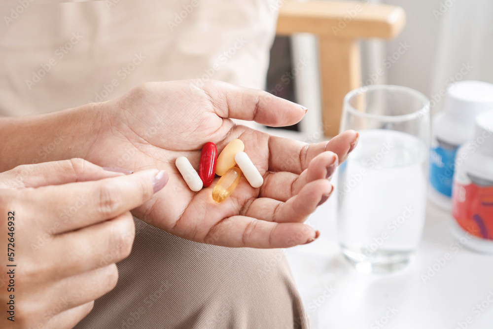 woman hand taking supplementary food, vitamins c, b, fish oil with a bottle of medicine, and a glass of water on a table woman hand taking supplementary food, vitamins c, b, fish oil with a bottle of medicine, and a glass of water on a table