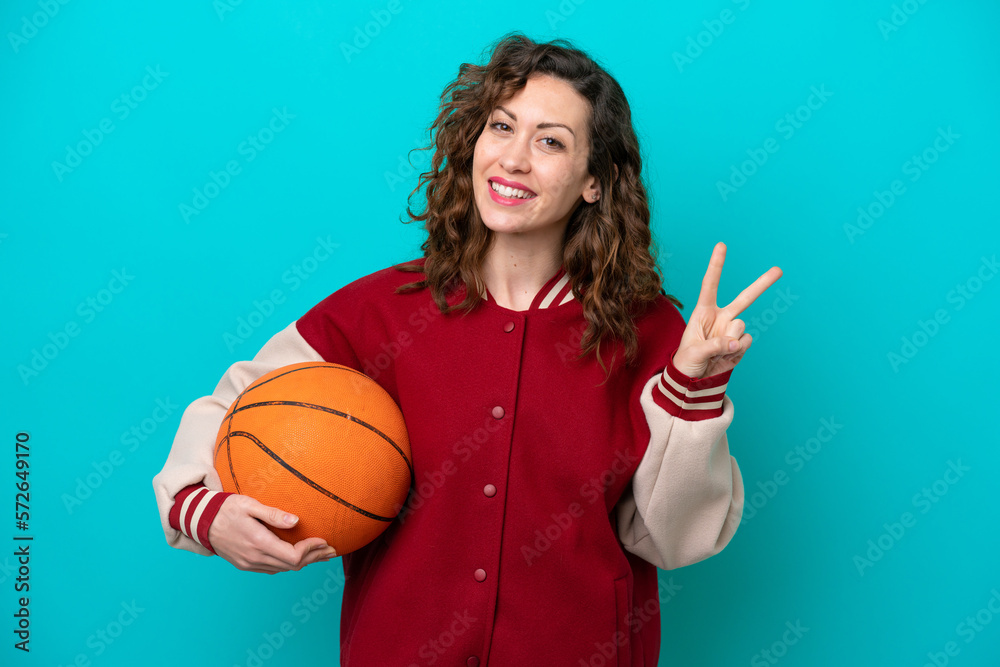 Young caucasian basketball player woman isolated on blue background smiling and showing victory sign