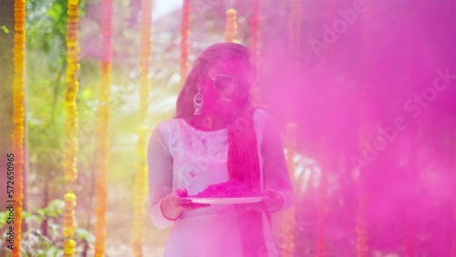 Happy young girl with sunglasses enjoys splashing holi podwer by looking camera on flower decorated background - concept of entertainment, ecstatic and freedom photo