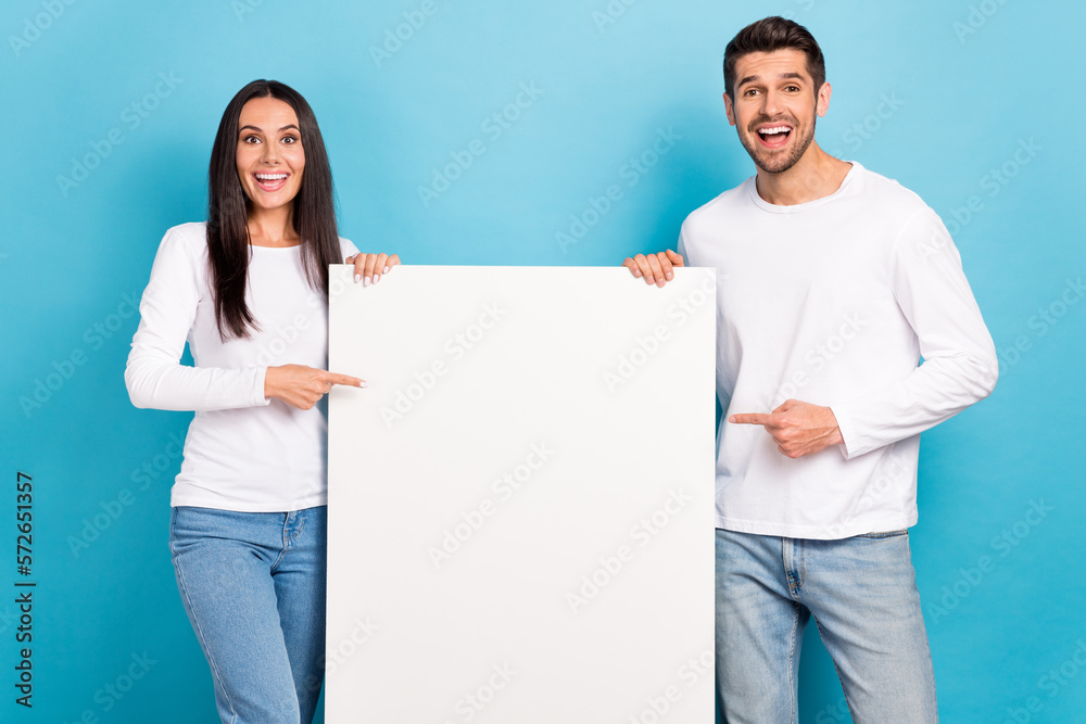 Portrait of two amazed positive people indicate finger empty space proposition isolated on blue color background Portrait of two amazed positive people indicate finger empty space proposition isolated on blue color background