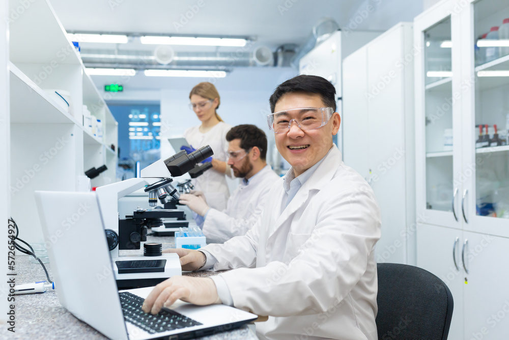 Portrait of asian lab technician, man with team group of people working in laboratory researching, man with microscope in white coat and goggles smiling and looking at camera. Portrait of asian lab technician, man with team group of people working in laboratory researching, man with microscope in white coat and goggles smiling and looking at camera.