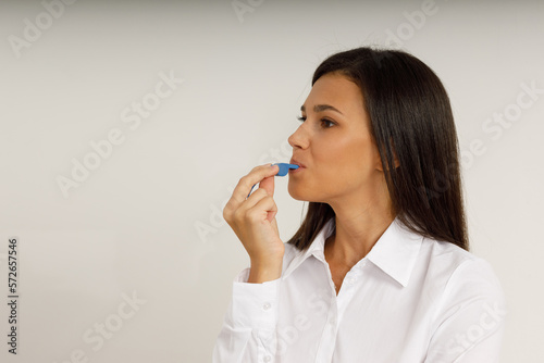 Portrait of attractive smiling girl brunette holding blue whistle in her hand and looking at the camera. Happy young woman with long hair in white shirt on isolated background. Fan, coach, counselor.