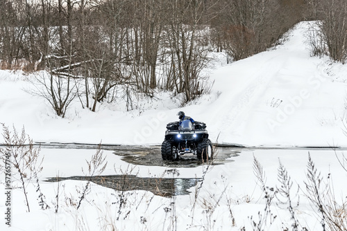 A man driving his ATV across the river in the wilderness at winter. © Andrey Nikitin