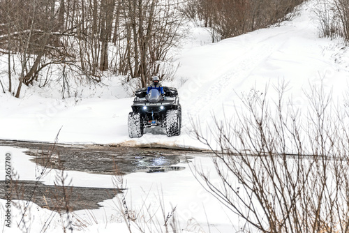 A man driving his ATV across the river in the wilderness at winter. © Andrey Nikitin