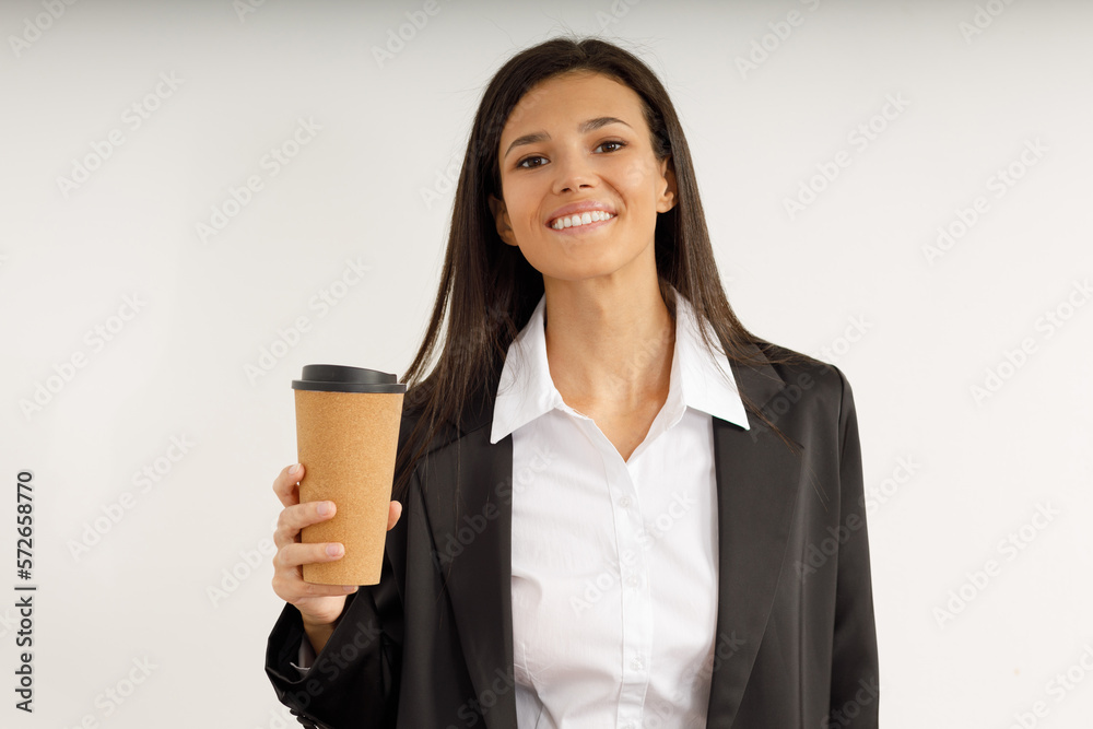 Portrait of happy pretty young woman in business suit holding paper cup of coffee in her hands on isolated white background. Studio shot of attractive brunette girl with snow-white smile. Portrait of happy pretty young woman in business suit holding paper cup of coffee in her hands on isolated white background. Studio shot of attractive brunette girl with snow-white smile.
