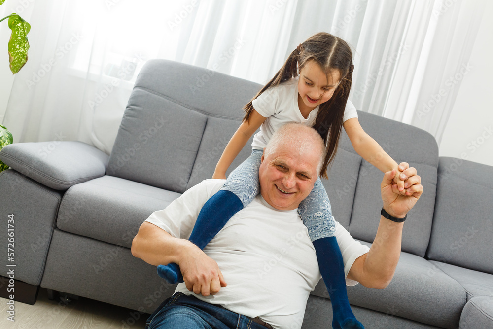 Cute little girl spending time with positive active grandpa in living room Cute little girl spending time with positive active grandpa in living room