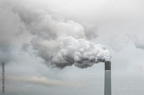 Thick and heavy smoke coming out of a huge and high chemical factory chimney under a misty and rainy sky
