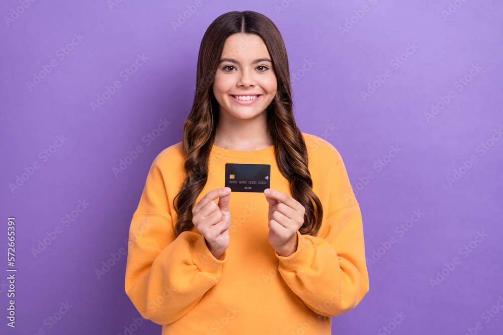 Photo of positive pretty lady wear orange sweatshirt holding credit card isolated violet color background Photo of positive pretty lady wear orange sweatshirt holding credit card isolated violet color background