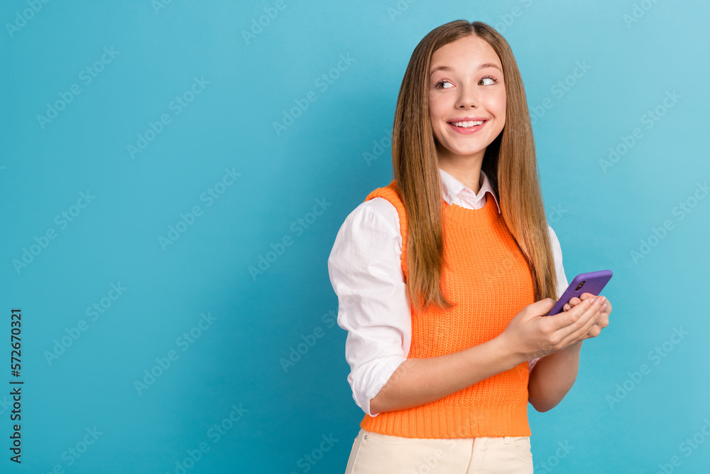 Photo of positive lovely girl hold telephone look empty space promotion isolated on blue color background Photo of positive lovely girl hold telephone look empty space promotion isolated on blue color background