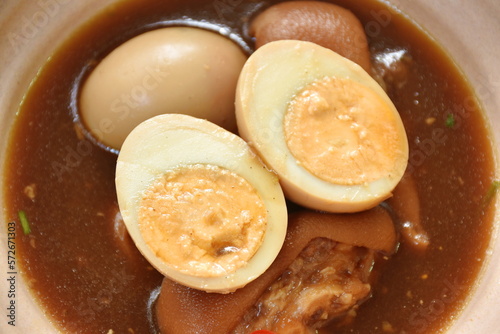 boiled half cut egg with fat pork leg in herb brown soup on bowl 