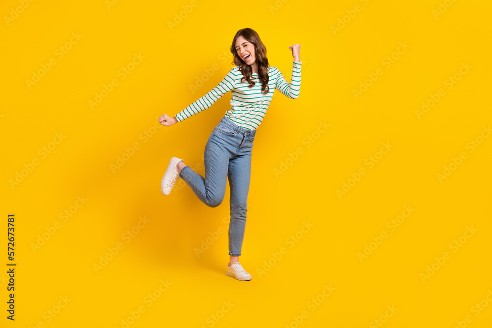 Full size photo of good mood crazy woman curly hairstyle striped shirt clenching fists having fun isolated on yellow color background