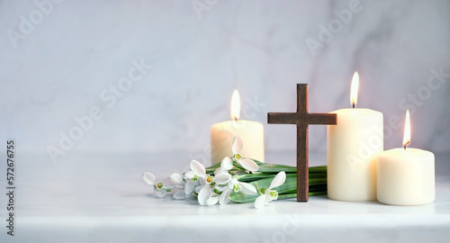 Wooden cross, snowdrops flowers and candles on table, blurred abstract background. Religious church holiday. symbol of faith in God, Christianity Feast, Easter, Palm Sunday, Lent