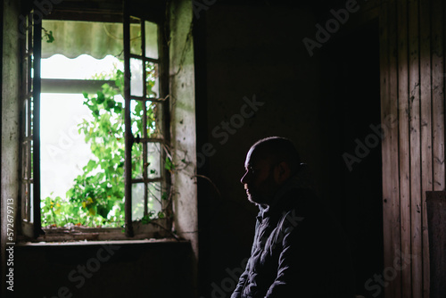 Silhouette of a man in an old uninhabitable house in front of a window. Depression, loneliness, despair, decline, sadness concept.