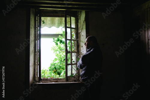 A man inside an old crumbling house near the window. Depression, loneliness, despair, decline, sadness concept. © Konstiantyn Zapylaie