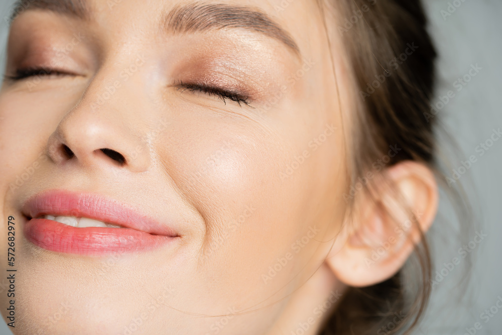 Close up view of pleased young woman with natural makeup closing eyes isolated on grey. Close up view of pleased young woman with natural makeup closing eyes isolated on grey.