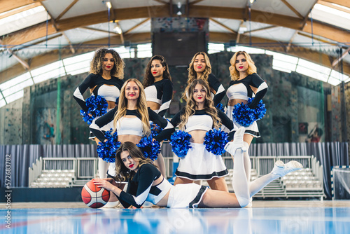 team of beautiful cheerleaders in black-white uniforms posing for the camera together, indoors. High quality photo