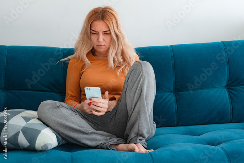Young Hispanic stressed woman sit on sofa in living room talks on smartphone looking concerned, listen bad news feels desperate, having unpleasant remote conversation, receive disagreeable information