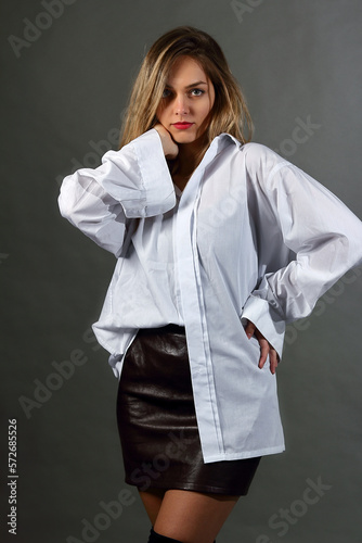 Young woman in a studio, in a shirt and a mini skirt, poses