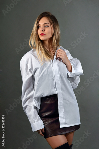 Young woman in a studio, in a shirt and a mini skirt, poses
