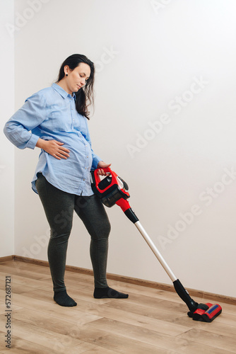 Pregnant woman cleaning floor with handheld vacuum cleaner. Young pregnant woman enjoys cleaning her house.