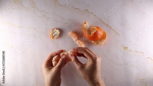 Womans hands peeling a clementine orange, top view on marble table