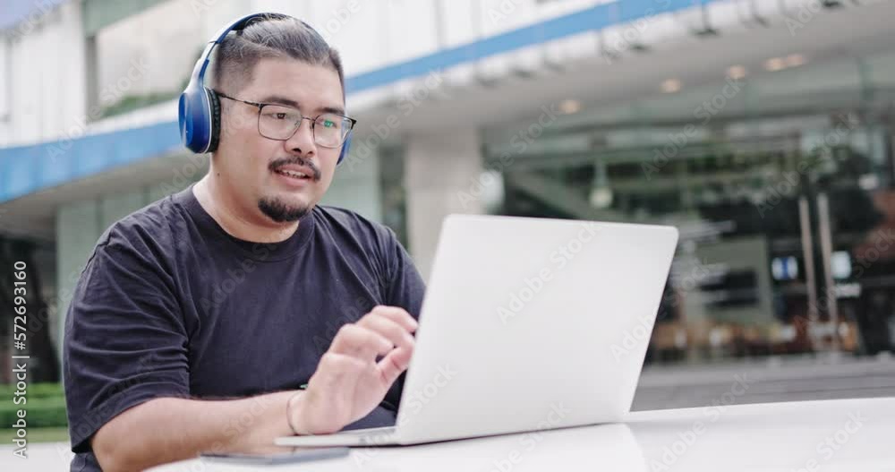Asian freelance working in headphones and working on laptop in the outdoors with high speed internet. Online meeting via video call and presentation work