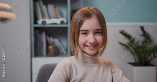 Close up of cute smart caucasian smiling girl loking at camera, indoors. Beautiful girlsitting at table at home with a laptop looks at camera and smiling photo