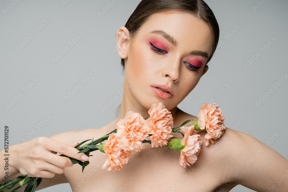 Fototapeta premium pretty woman with pink visage holding fresh carnations near bare shoulder isolated on grey.