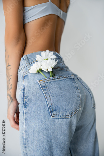 partial view of woman in bra posing with white flowers in back pocket of jeans isolated on grey. © LIGHTFIELD STUDIOS