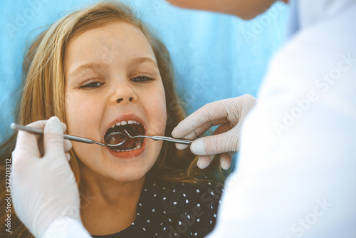 Little baby girl sitting at dental chair with open mouth during oral check up while doctor. Visiting dentist office. Medicine concept. Toned photo
