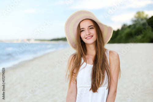 Portrait of a happy smiling woman in free happiness bliss on ocean beach standing with a hat. A female model in a white summer dress enjoying nature during travel holidays vacation outdoors © rogerphoto