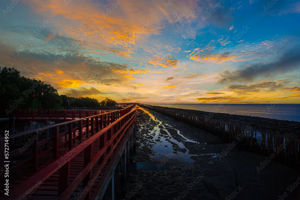 Scenery of the wooden bridge at sunrise,red wooden bridge and sea in the morning,In the morning the red bridge and the sun rise on the horizon. Bridge over the sea in Thailand Thai landscape.