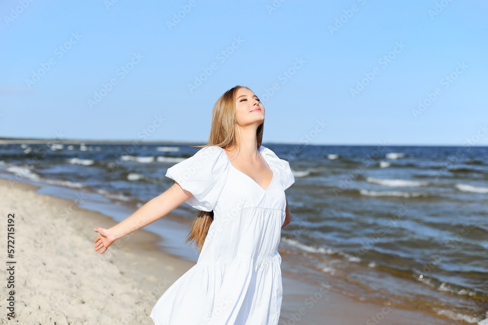 Happy smiling beautiful woman is on the ocean beach in a white summer dress, open arms Happy smiling beautiful woman is on the ocean beach in a white summer dress, open arms